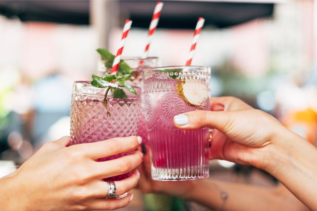 Glasses of vibrant drinks being raised for a toast in a lively setting. Public drinking has its limits in Singapore, with strict regulations on where and when it’s allowed, ensuring a safe and orderly environment.