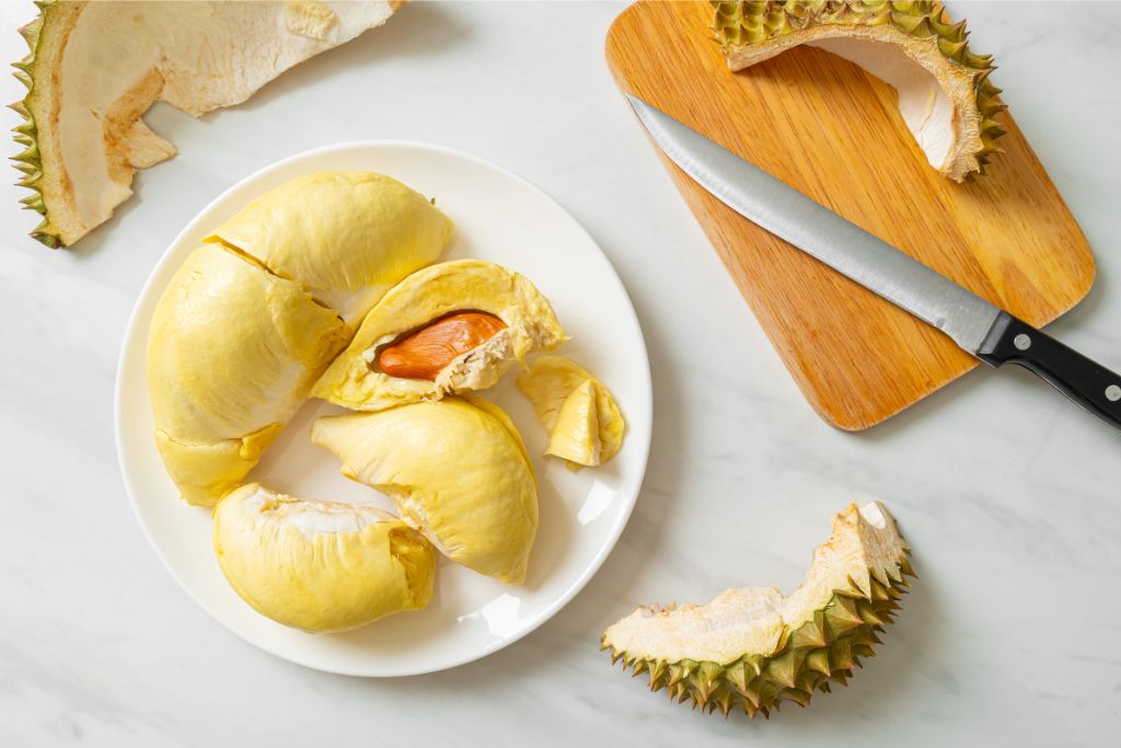 A plate of bright yellow durian fruit, alongside its spiky shell, sits on a table. This beloved yet pungent fruit is banned on Singapore’s public transport—a quirky travel rule every visitor should remember.