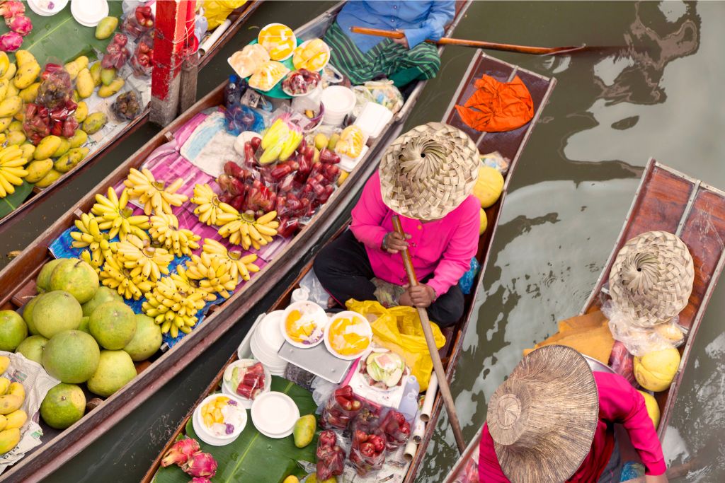 A vibrant floating market in Thailand with vendors selling tropical fruits from small boats. One of the reasons to travel to Thailand is its unique market experiences, making it a great place to visit.