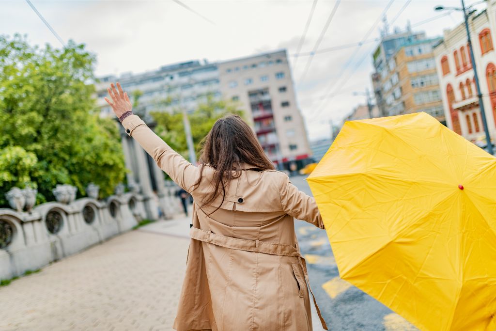 A woman walking through a city street holding a bright yellow umbrella while wearing a beige trench coat. Captures Singapore's unique winter aesthetic and style.