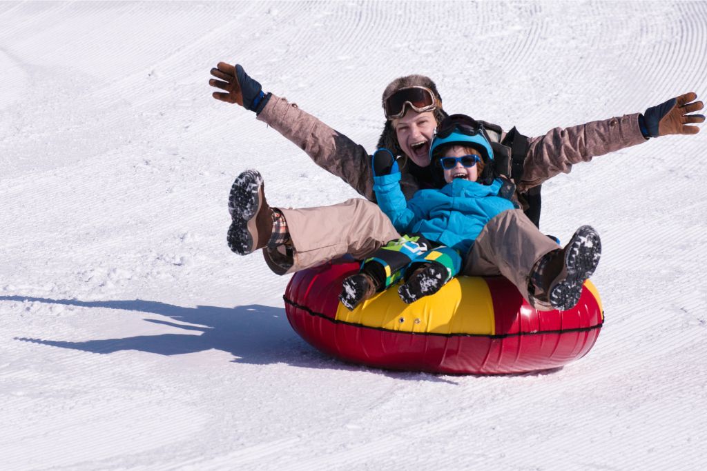 A parent and child enjoying a thrilling snow tubing ride on a snowy slope, sharing laughter and excitement. Perfect for snowy winter getaways and family-friendly winter adventures.