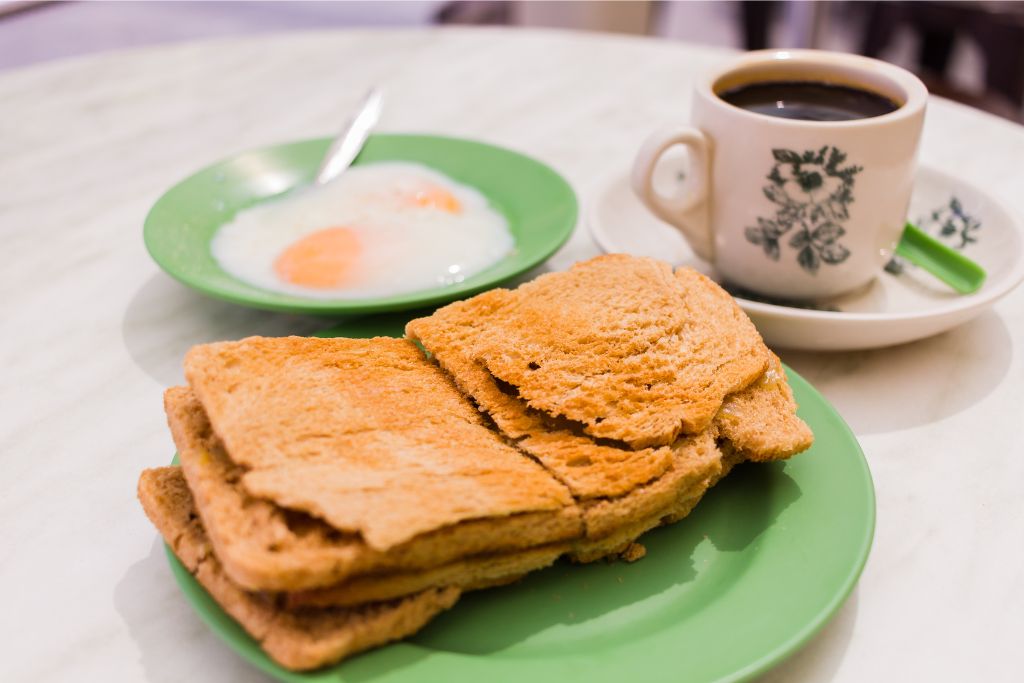 A plate of golden-brown kaya toast with soft-boiled eggs and a cup of traditional black coffee. A cozy meal to enjoy during Singapore’s winter mornings.