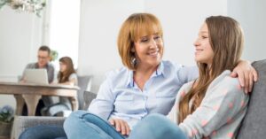 Teen girl smiling while chatting with her mom on the couch, representing trust-building and open communication—essential strategies for how to convince your parents to let you travel alone
