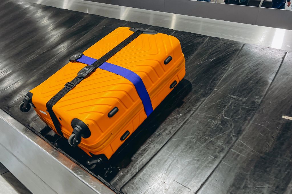 Bright orange suitcase with a blue strap on an airport baggage carousel, symbolizing independence, airport safety, and preparation—core points when addressing how to convince your parents to let you fly alone.