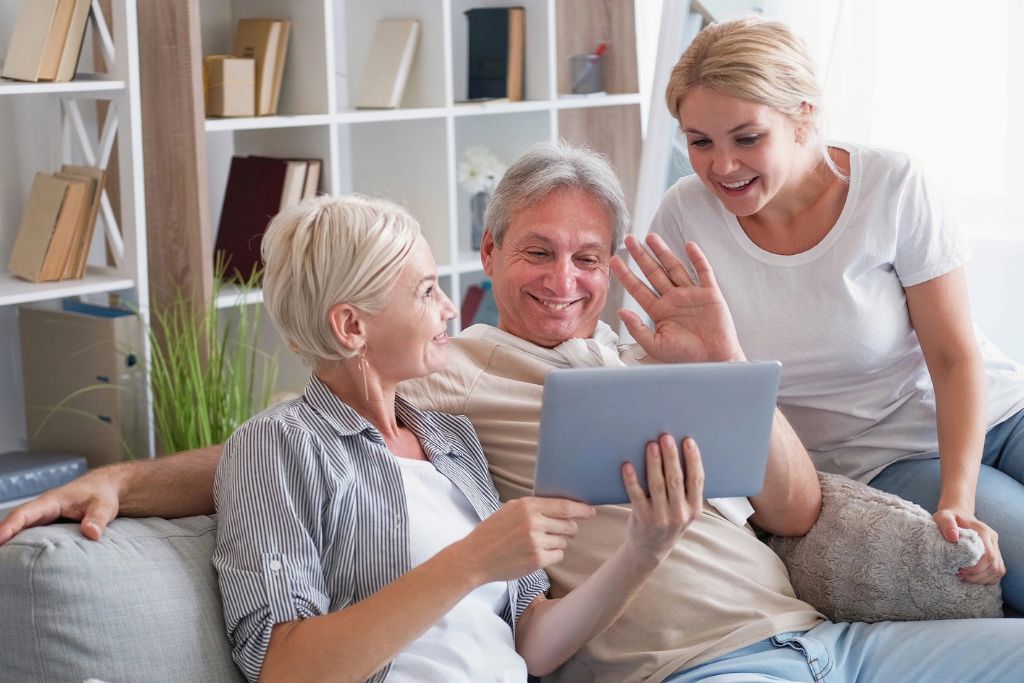Smiling woman video chats with her parents on a tablet while sitting on a couch—showing how staying connected is a key tactic in solo travel safety tips and earning your parents’ trust for solo travel.