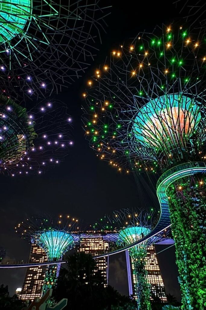 Supertrees sparkle in green, gold, and purple lights during the Gardens by the Bay light show, with the Marina Bay Sands hotel glowing behind. This nightly event, known as Garden Rhapsody, is one of the most visually stunning light shows in Singapore.