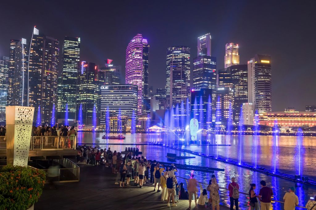 Crowds watch the Spectra light and water show from the Marina Bay waterfront as blue and purple lights dance across the water in front of the illuminated skyline. This nightly event is one of the top light shows in Singapore and a free attraction for all ages.