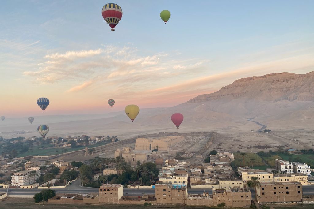 Colorful hot air balloons float above an ancient village in a vast desert landscape during sunrise—an inspiring visual for the best solo travel spots and a dream destination to include when convincing your parents to let you go somewhere.