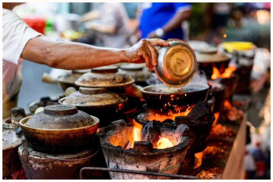 A hawker preparing claypot dishes over open flames. This scene captures the vibrant atmosphere of the best hawker centers in Singapore and features some of the best street food in Singapore.