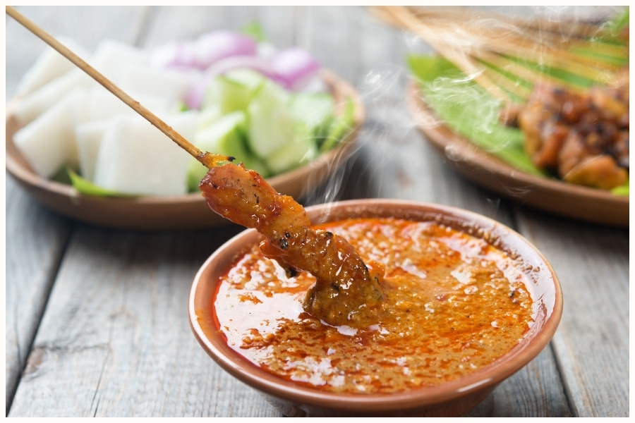 close-up of satay skewers being dipped into a rich peanut sauce. This image highlights one of the must-try hawker foods in Singapore, found at various food courts in Singapore.