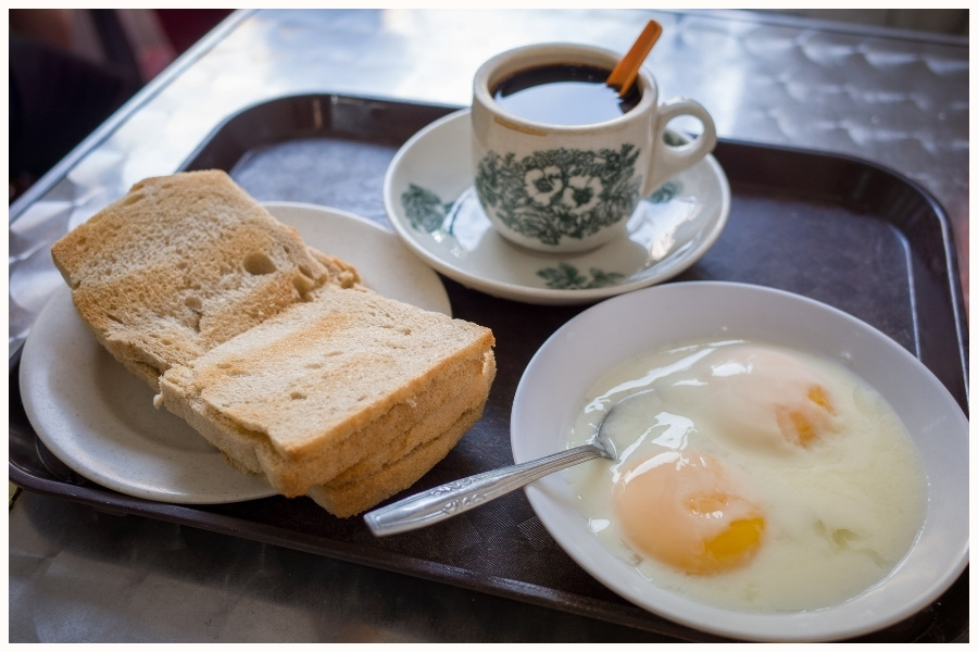 Traditional kaya toast, soft-boiled eggs, and a cup of coffee. This classic hawker breakfast captures the essence of Singapore eats and what to eat in Singapore for a local experience.