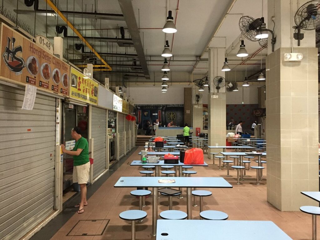 n almost empty hawker center with a few vendors preparing to open. This image depicts the calm before the rush at one of the most famous hawker centers in Singapore, known for its affordable and diverse food options.