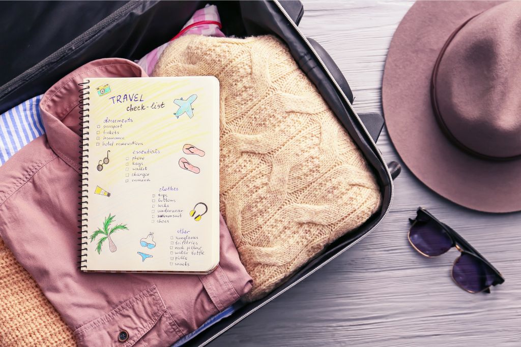 A neatly packed suitcase with a travel checklist. The list includes items like documents (passport, tickets, insurance), essentials (phone, keys, wallet, charger), clothes, and toiletries. This image highlights packing tips for girls and emphasizes how to avoid overpacking for a trip or vacation.