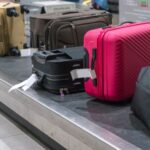 A bright pink suitcase is easily noticeable on an airport baggage carousel, surrounded by darker, more traditional luggage. Choosing bold colors like pink is an effective way to make your luggage stand out and simplify identification