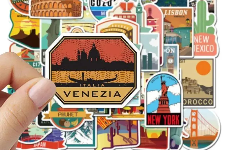 A hand holds a colorful 'Venezia' sticker, with a backdrop of various travel destination stickers, perfect for decorating luggage. Using stickers from different places is a creative way to make your luggage unique and easily identifiable.