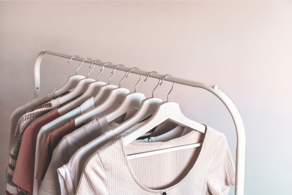 Clothes neatly hanging on a rack, displaying organized outfits in neutral tones. This visual suggests a minimalistic approach, offering ideas on how to stop overpacking by selecting versatile clothing options. Perfect for tips on what not to pack for a trip to avoid overpacking.