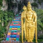 The vibrant rainbow-colored steps leading up to Batu Caves temple, with the towering golden Lord Murugan statue in the foreground. Batu Caves, located near Kuala Lumpur, is famous for its colorful steps and attracts visitors for its cultural and religious significance.