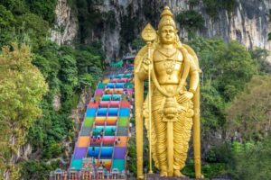 The vibrant rainbow-colored steps leading up to Batu Caves temple, with the towering golden Lord Murugan statue in the foreground. Batu Caves, located near Kuala Lumpur, is famous for its colorful steps and attracts visitors for its cultural and religious significance.