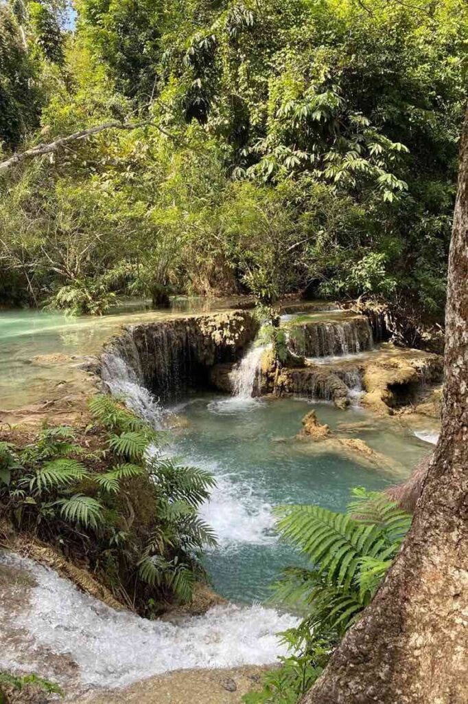 A beautiful scene of Kuang Si Waterfall surrounded by lush greenery in Laos, with turquoise waters cascading down multiple tiers. A perfect fall destination in Asia for nature lovers seeking serene fall trips to explore Asia’s natural beauty and hidden gems.