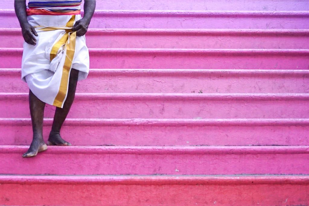 A man dressed in traditional attire stands on the iconic pink steps of Batu Caves in Kuala Lumpur, Malaysia. The 272 colorful steps lead to the Batu Cave temple, a major Hindu site and top attraction for visitors on Batu Cave tours.