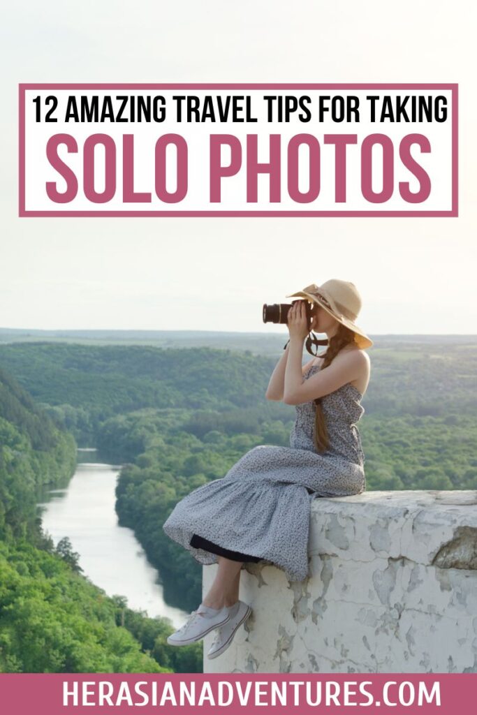 A solo traveler sits on a rock ledge overlooking a lush green valley, holding a camera and taking solo travel photos, with a guide on how to take your own pictures while traveling alone. 