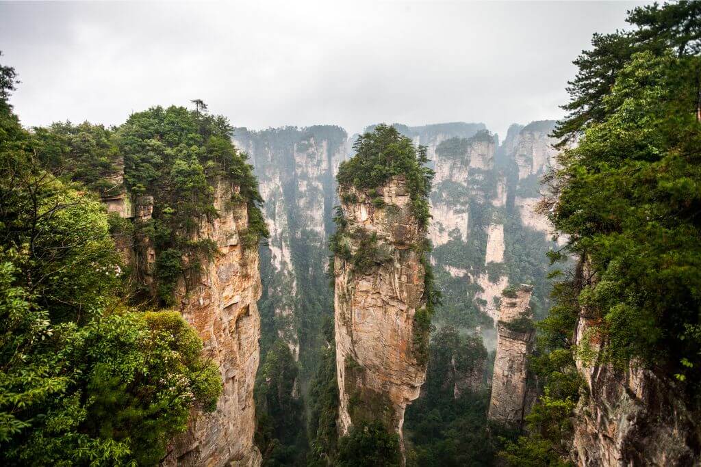 The dramatic sandstone pillars of Zhangjiajie National Forest in China, rising above lush greenery in the misty autumn air. This UNESCO World Heritage Site is a must-see place in Asia during the fall season, offering breathtaking autumn landscapes and one of the best fall travel destinations for nature lovers visiting Asia.