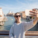 Solo traveler taking a selfie on a scenic bridge in Venice, showing how to take travel photos of yourself on iconic landmarks.