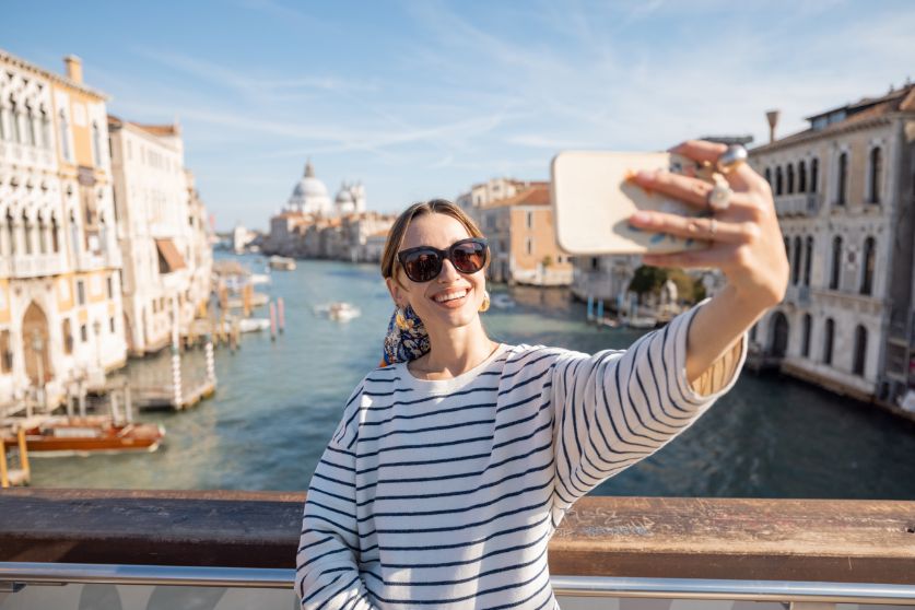 Solo traveler taking a selfie on a scenic bridge in Venice, showing how to take travel photos of yourself on iconic landmarks.