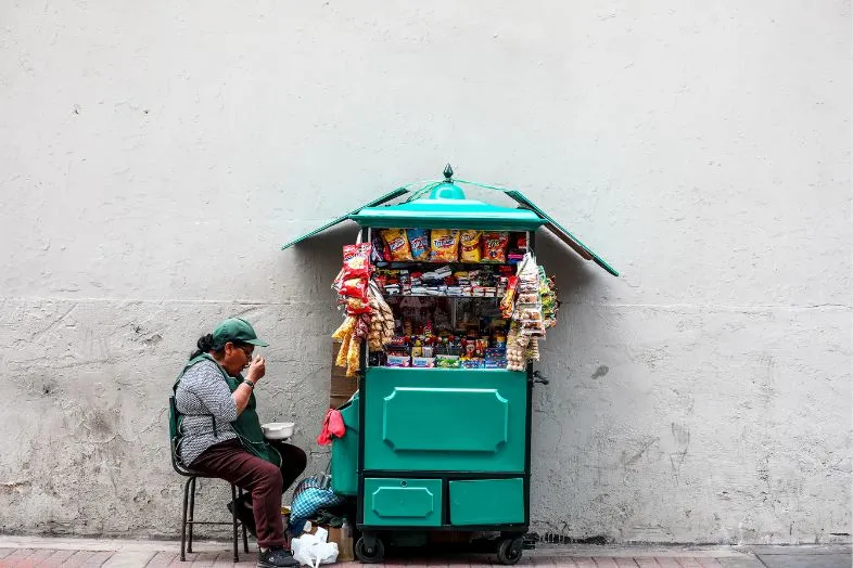 A street vendor in Southeast Asia selling snacks and goods. Cash is the primary method of payment at local markets like this, where credit cards are typically not accepted.