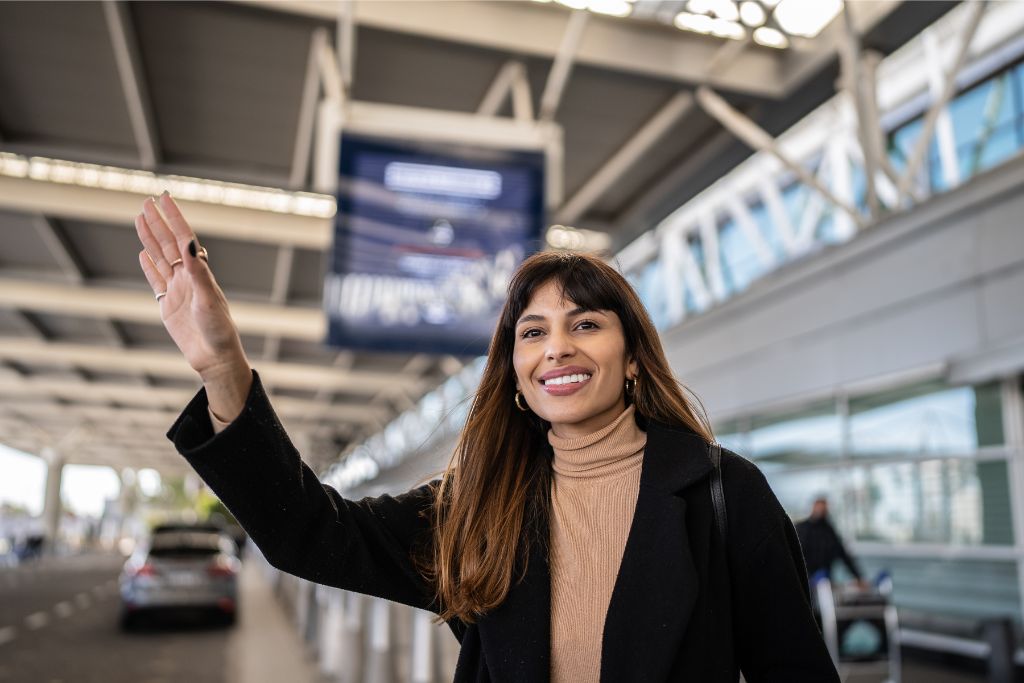 Smiling woman waving at the airport terminal. Tips for first-time flyers on how to prepare for solo travel and what to expect during their first flight experience.