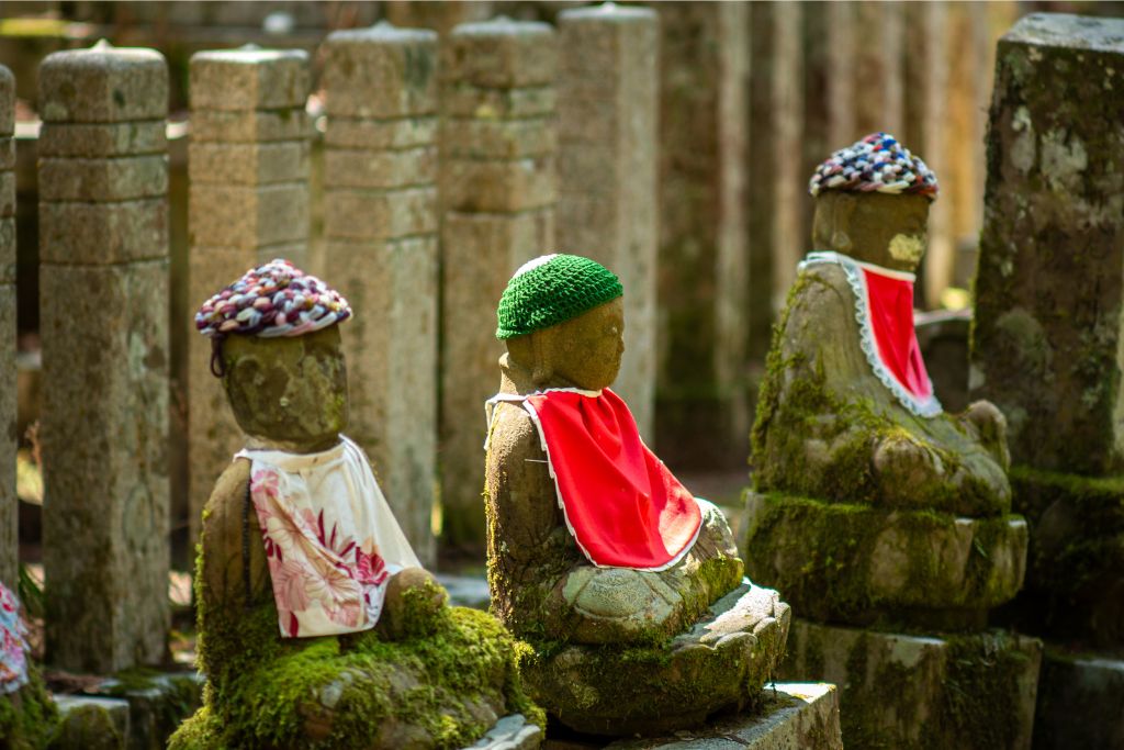 Moss-covered stone statues dressed in red bibs, located in a quiet forest in Japan. A spiritual and peaceful place to visit during the fall season, showcasing Japan's unique cultural heritage amidst beautiful autumn foliage.