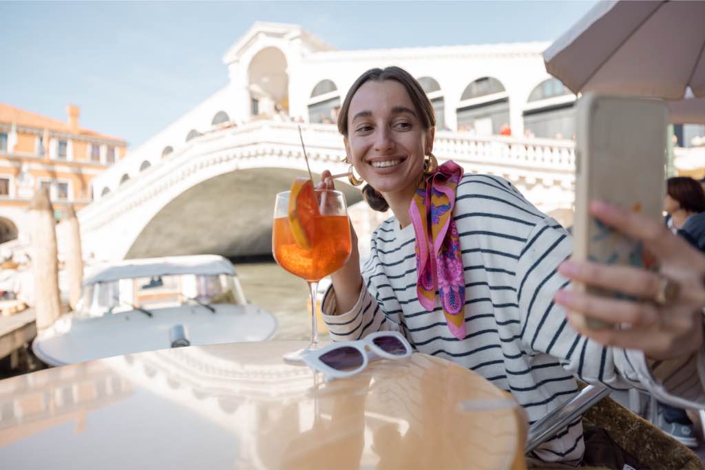 Solo traveler enjoying a drink at a Venetian cafe while taking a selfie, demonstrating how to take Instagram-worthy photos on your own.