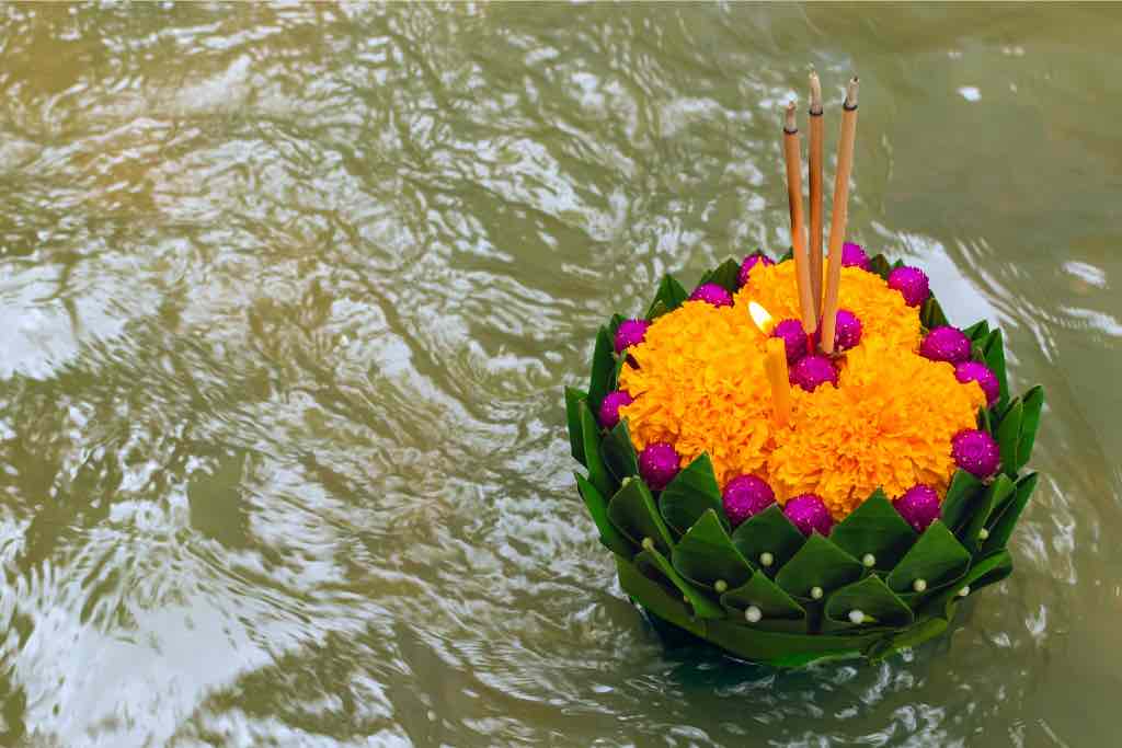 A floating krathong made of banana leaves, marigold flowers, and incense sticks drifting in the water during the Loy Krathong Festival in Thailand. This traditional festival, celebrated in autumn, is one of the best cultural experiences in Asia during the fall season, making it a must-see event for travelers exploring Asia in fall.