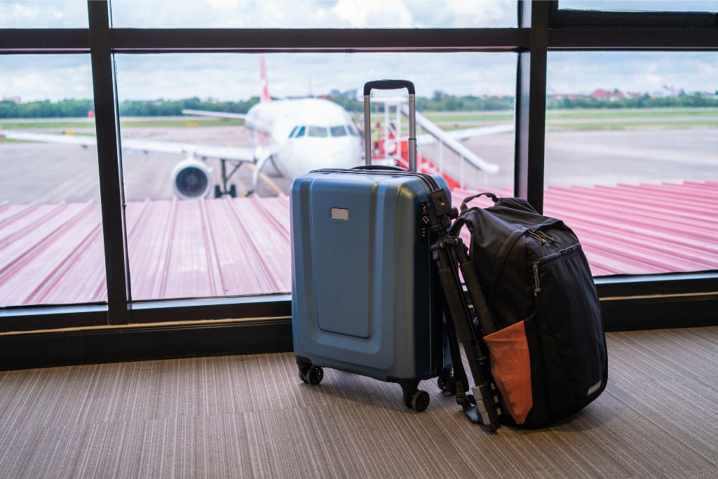 Two suitcases placed near a window with a plane visible outside. First-time flyer tips for packing and what to expect when waiting at the gate before boarding your flight.