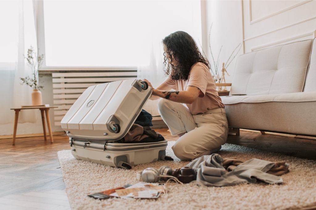 A person packing a suitcase in a tidy room, preparing for a trip. The careful packing technique shown here suggests effective packing tips for girls, offering guidance on how to avoid overpacking by using smart organization strategies.