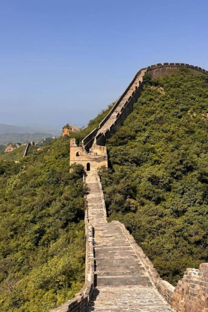 The Great Wall winds over green hills under a clear blue sky. Visiting this UNESCO site is one of the best fall destinations in Asia and a must for those exploring Asia in October.