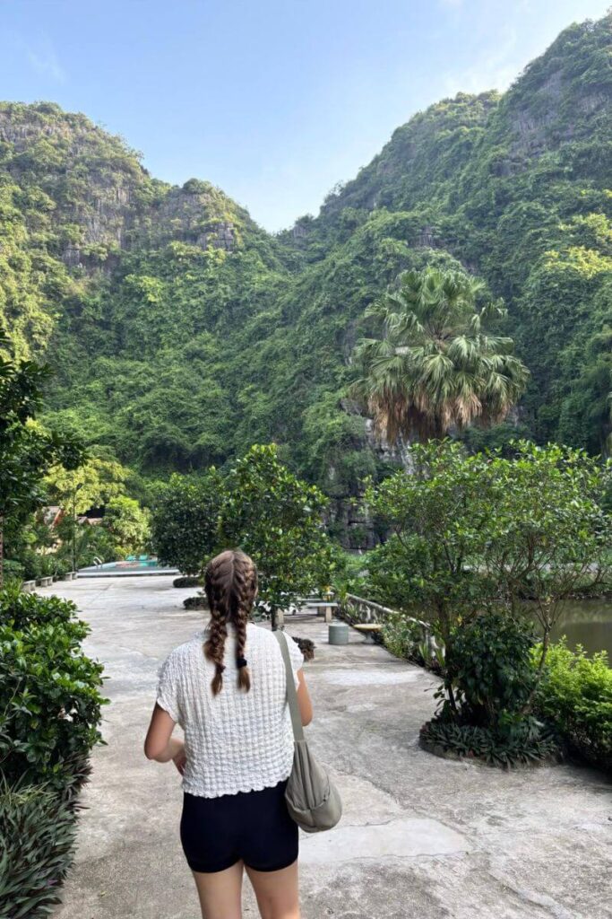 A traveler with braided hair walks through lush greenery in Ninh Binh, surrounded by limestone peaks. This tranquil landscape makes for a perfect autumn in Asia escape and a scenic fall destination in Asia.
