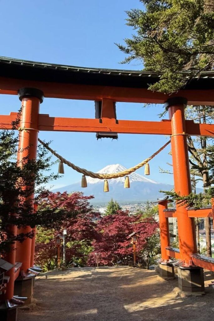 A bright red torii gate frames Mount Fuji in the distance, surrounded by red autumn leaves and clear skies. This view defines autumn in Asia and ranks among the best fall destinations in Asia.