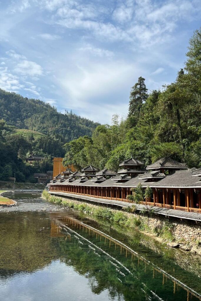 Traditional covered wooden bridges stretch over a calm river with forested hills in the background. This charming riverside view captures autumn in Asia and showcases one of the most scenic Asia fall destinations.