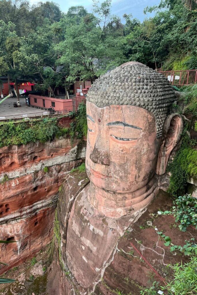 The massive stone-carved Leshan Buddha sits amid cliffs and greenery in Sichuan, China. A spiritual wonder and one of the most awe-inspiring fall destinations in Asia for an Asia autumn getaway.