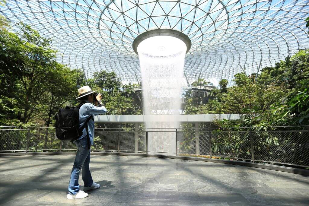 A tourist photographs the stunning indoor waterfall at Jewel Changi Airport, Singapore. A great reason to visit Singapore, this unique attraction showcases why Singapore is worth visiting and makes it a top holiday destination.