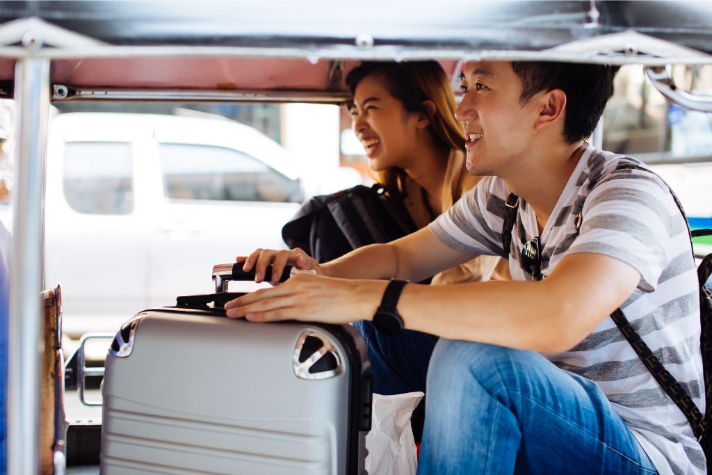 A smiling couple inside a tuk tuk with luggage, experiencing the fun and convenient way to travel Sri Lanka. Renting a tuk tuk in Sri Lanka is a great option for a cheap holiday or backpacking adventure.