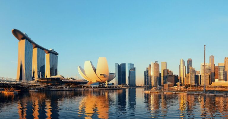 A golden sunset reflects on the water in front of Marina Bay Sands and the Singapore skyline. This iconic view is one of the top reasons to visit Singapore, showcasing why Singapore is worth visiting for its stunning modern architecture and waterfront scenery, making it a memorable holiday destination.