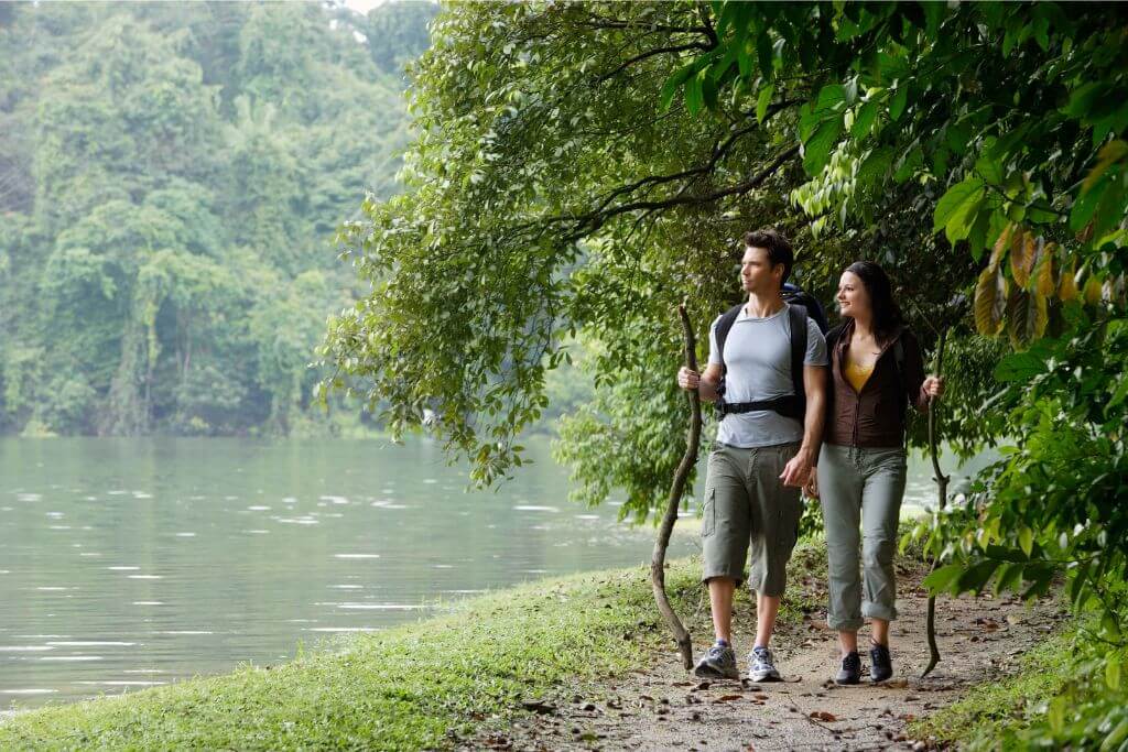 A couple enjoys a peaceful walk along a nature trail beside a lake in Singapore. The city's balance of green spaces and urban life is one reason Singapore is a nice place to visit, making it worth visiting for nature enthusiasts.