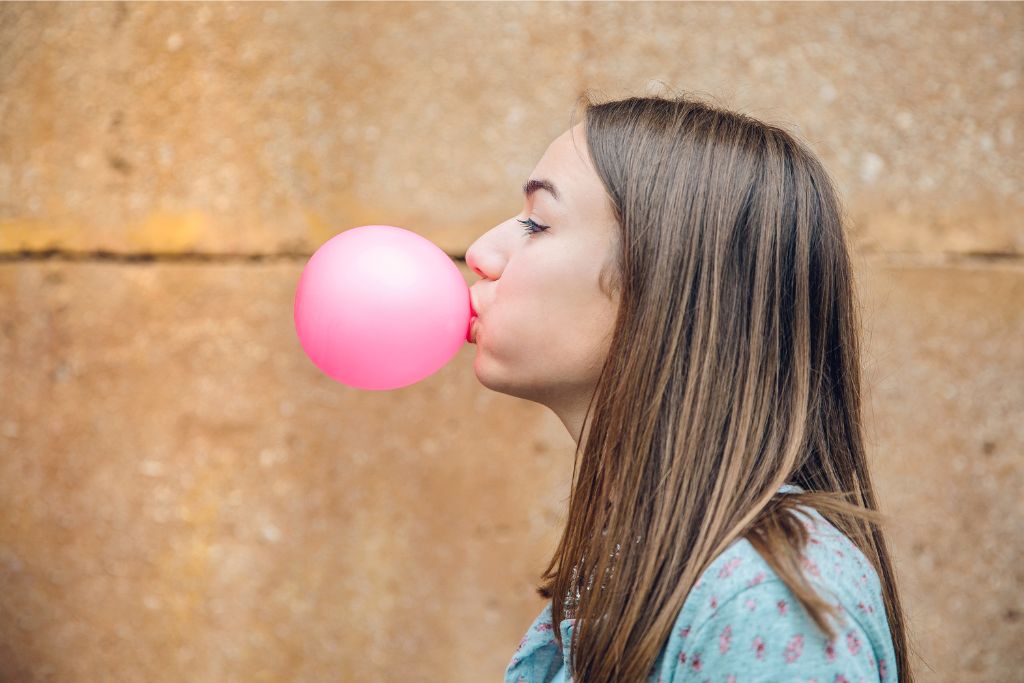 A woman blows a pink bubble gum bubble, a nod to Singapore's strict regulations against chewing gum. This image reflects one of the reasons not to visit Singapore for some, but also adds to its distinctive appeal.