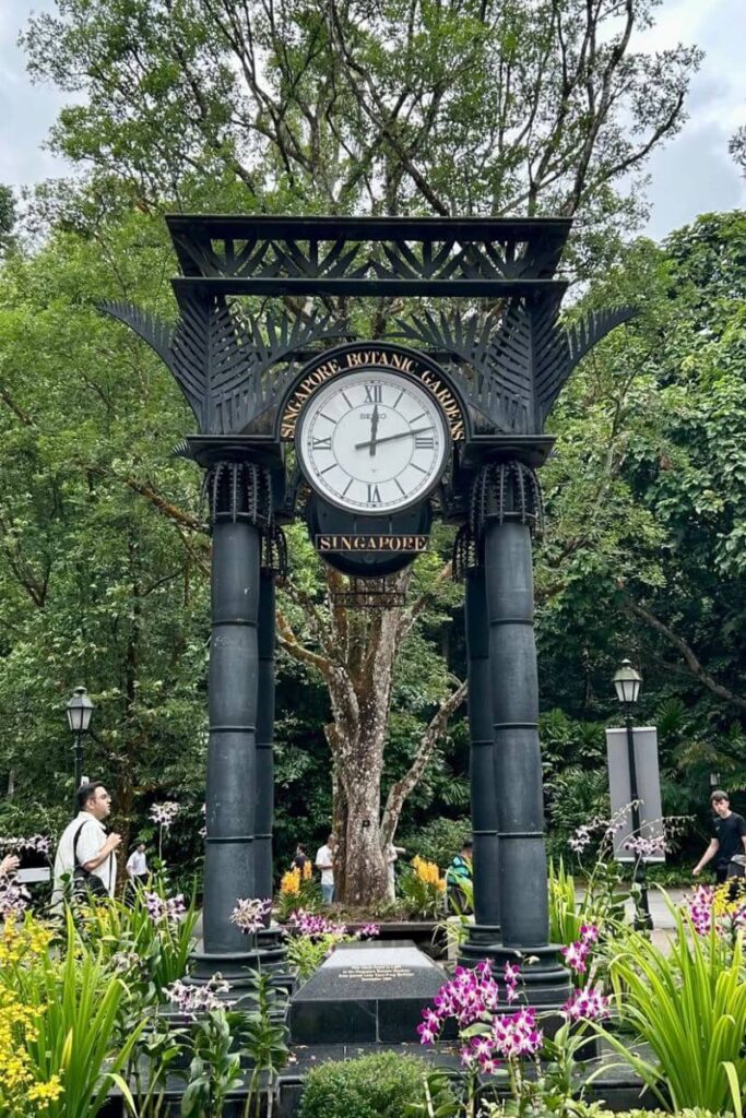 Black metal clock structure labeled “Singapore Botanic Gardens” stands among orchids and tall trees in the country’s only UNESCO World Heritage site. The peaceful gardens are a reason why Singapore is worth visiting with kids or anyone looking for nature in the city.