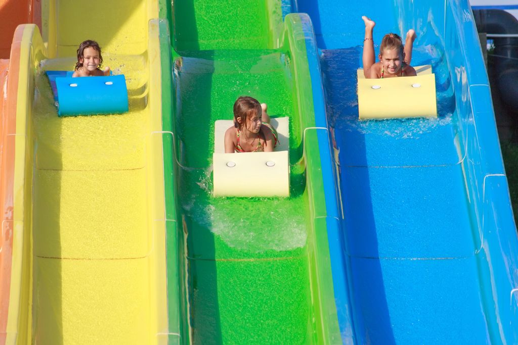 Three smiling girls ride down yellow, green, and blue water slides on mats at a Singapore waterpark. For families wondering if Singapore is worth visiting with kids, this fun attraction is a clear yes.