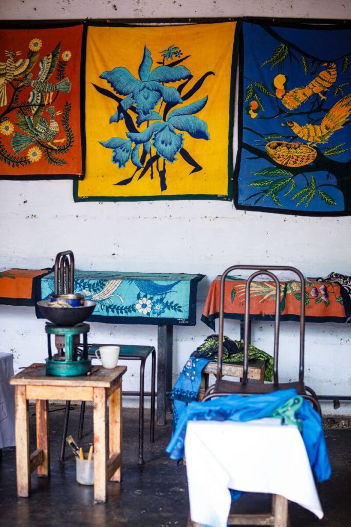 A display of vibrant batik tapestries with floral and bird designs, hanging in a Sri Lankan artisan’s workshop. These handcrafted textiles make perfect gifts from Sri Lanka, representing local artistry and culture.