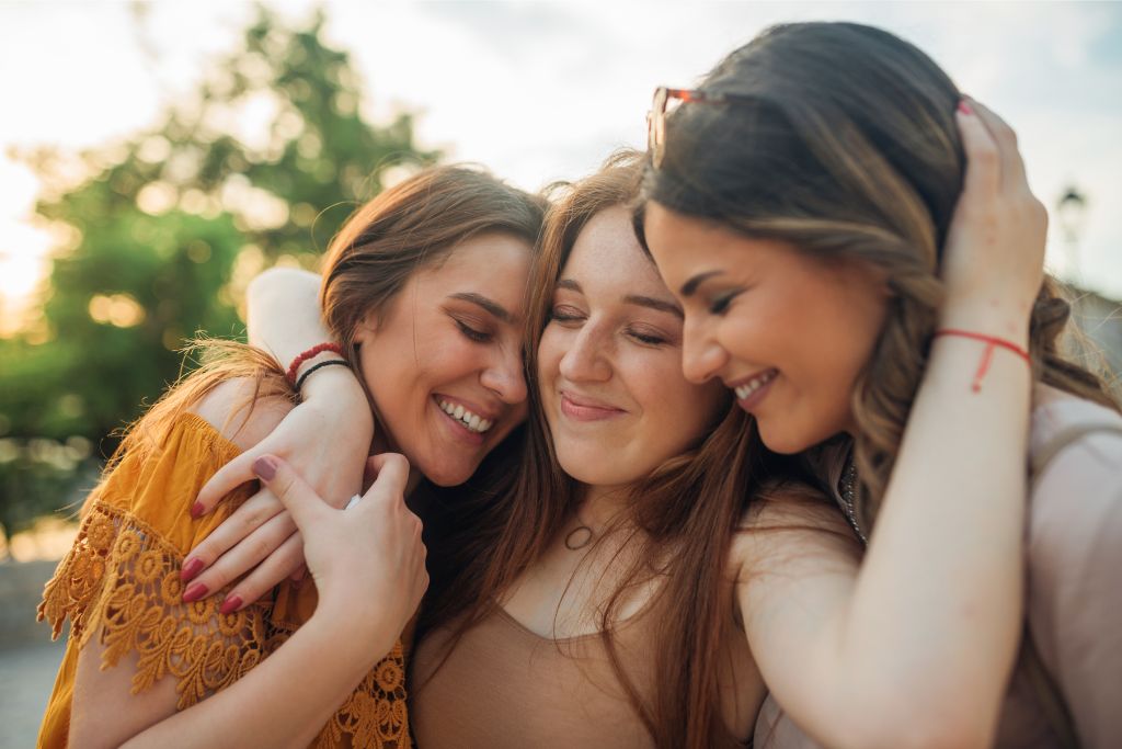 Three women sharing a joyful embrace outdoors, capturing the essence of bonding and unforgettable moments during a Southeast Asia honeymoon or backpacking trip.