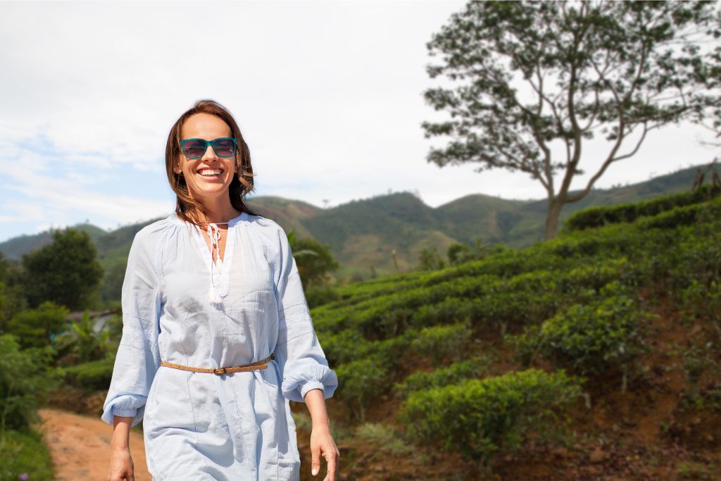 miling woman walking through a tea plantation in Sri Lanka’s lush landscape, illustrating the best time to go to Sri Lanka for scenic hill country tours.